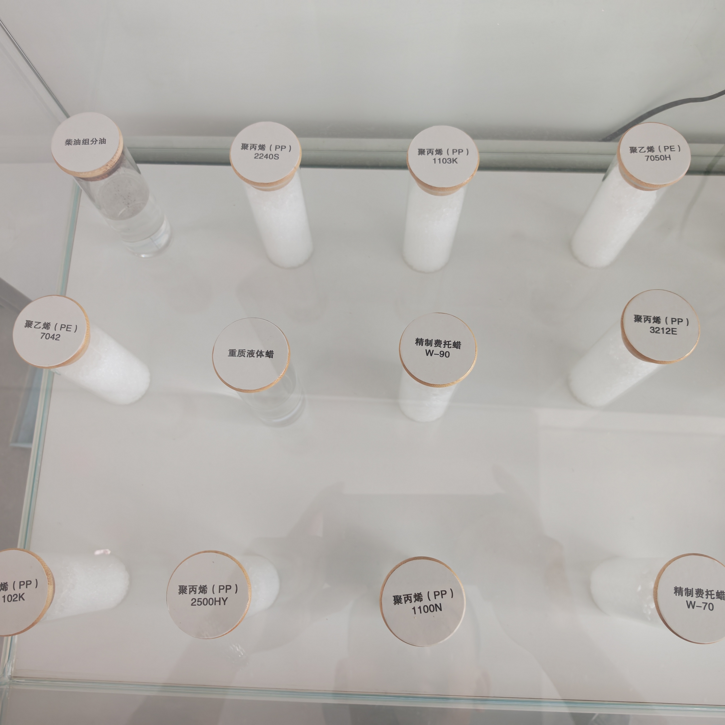 Glass display case with labeled test tubes of SNCC coal-based PP, PE resin pellets and refined Fischer-Tropsch wax samples
